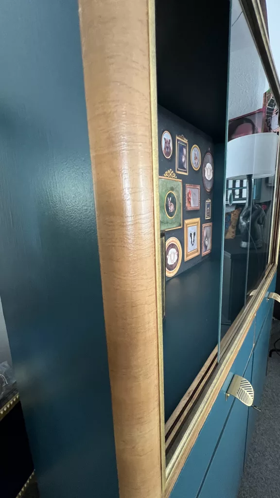 Detail: Holzkante und Glasfront der Vitrine mit Blick auf die Bilderwand