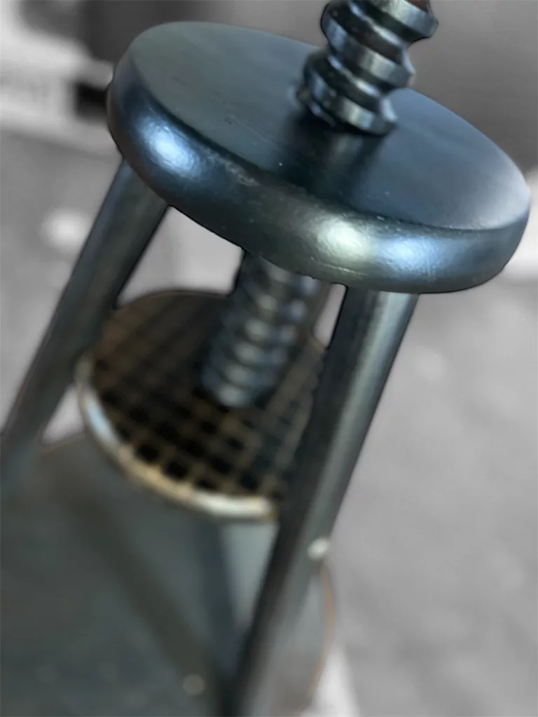 Detail an Polly: schwarze Spindel und das durchbrochene Metallband am Gestell