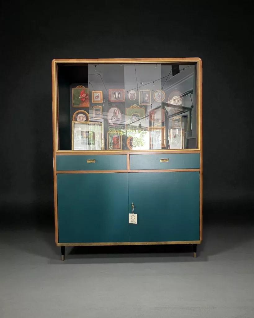 Angelikas Vitrine von vorn: petrolfarbener Korpus mit Holzrahmen und Tierporträts hinter Glas