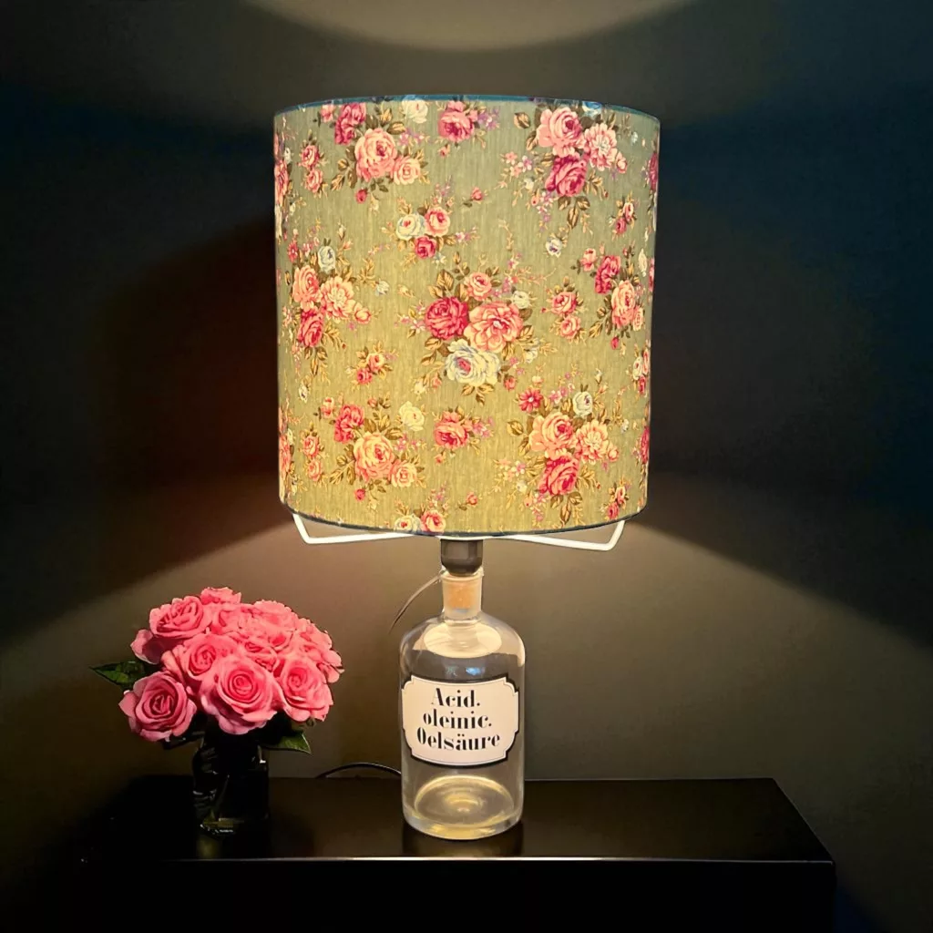 Flaschenlampe mit Rosenschirm, daneben ein Strauß Kunstblumen